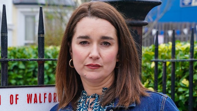 Vicki Fowler standing next to the Albert Square sign in EastEnders.