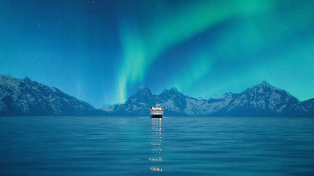 Hurtigruten's MS Nordkapp sailing into the distance with the Northern Lights dancing in the sky.
