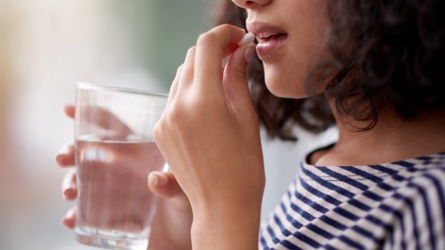 Woman taking painkiller with a glass of water.