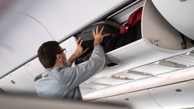 Man putting luggage into overhead locker on airplane. Traveller placing carry on bag in overhead compartment