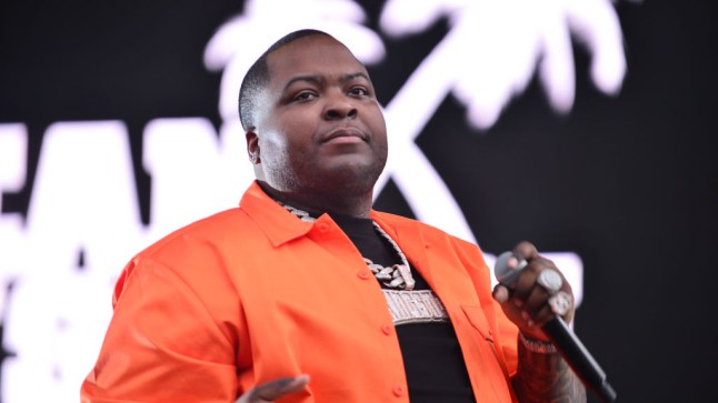 Sean Kingston in orange shirt stands on stage holding microphone