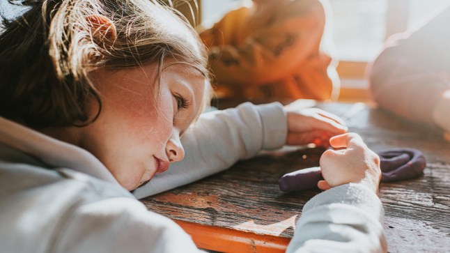 A young girl in preschool puts her head down on the desk and pouts