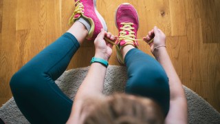 Young sporty woman with smart watch tying shoelaces