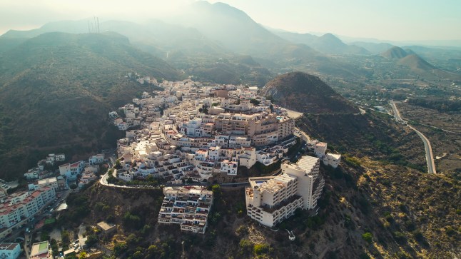 Aerial view of Mojacar, Spain, with its white buildings on top of a hillside surrounded by green mountains.