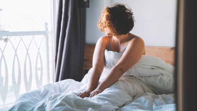 Good morning weekend. Woman wake up and sit in bed looking to the window