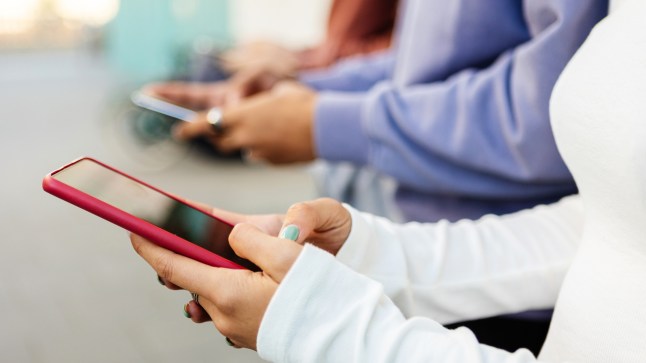 Close up view of young teenage people using cellphones standing outdoors