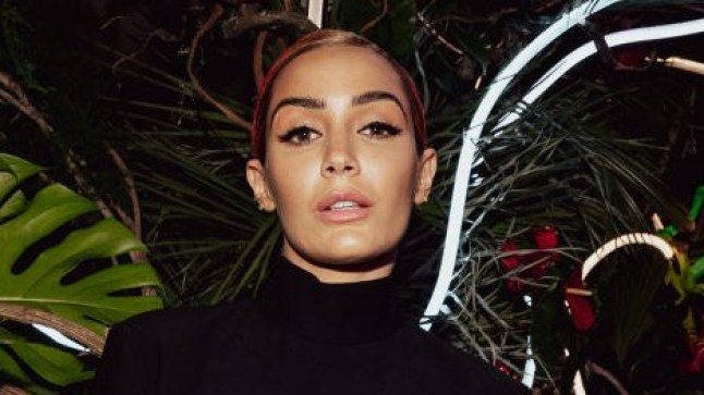 Frankie Bridge posing in front of a floral backdrop at the 2023 Baftas. She is wearing a black dress with cutouts on her sides