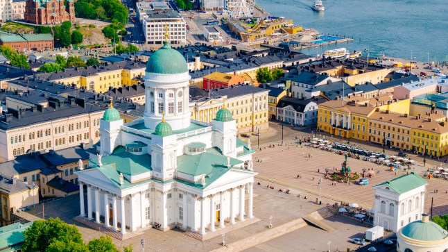 Aerial view of the white Helsinki Cathedral with its turquoise domed roof, on a sunny day, surrounded by buildings and near the water.
