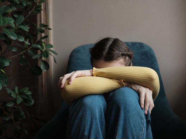 Upset depressed teenager crying at home, sad frustrated teen girl sitting by window with head on knees. Teenagers and mental health concept