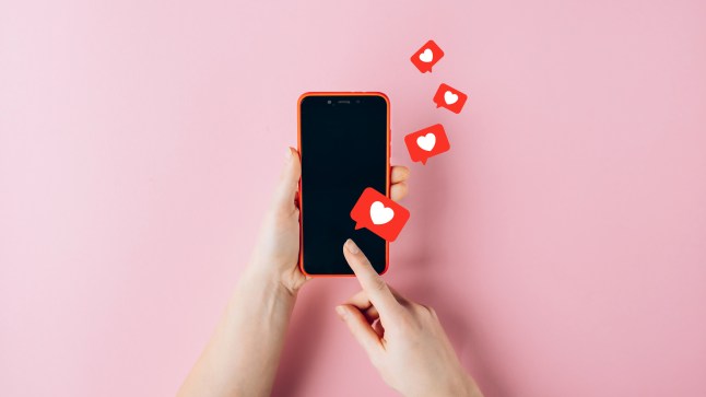Female hands holding red mobile phone with many social media likes on pink background