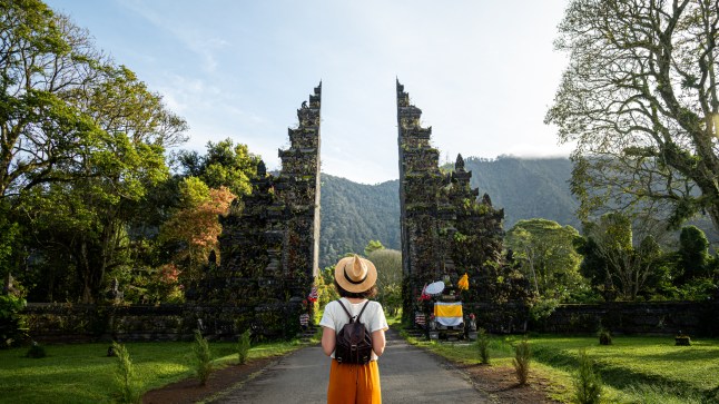 Woman traveler with backpack enjoying Balinese Hindu temple entrance.