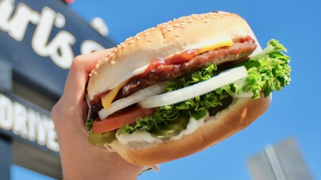 A hand holding a burger in front of a Carl's Jr. sign