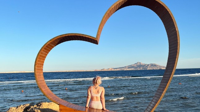 Jessica Lindsay sitting in a heart-shaped wooden structure in front of the sea in Egypt.