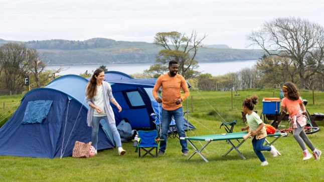 A shot of a mid adult mother and father in nature with their two young daughters. Both young girls are running around and having fun, they are camping overnight in a tent in Scotland.
