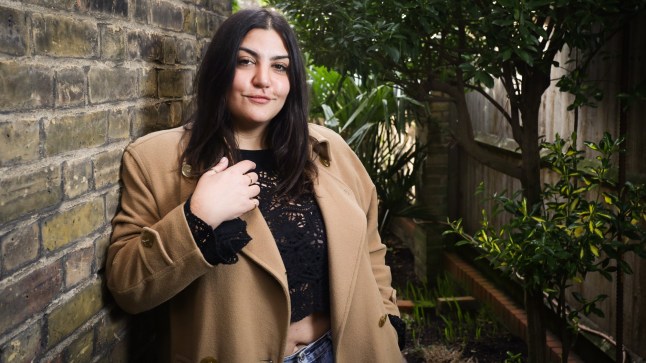 Almara Abgarian standing outside by a brick wall; a wooden fence with trees/flower boxes on her other side (Picture: Rachel Adams 2023)