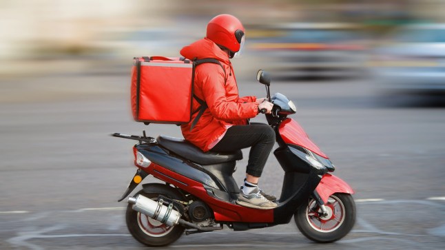 Food delivery moto scooter driver with red backpack behind back is on his way to deliver food. Courier on scooter delivering food. Quick shipping of goods to customers; Shutterstock ID 1730162416; purchase_order: -; job: -; client: -; other: -
