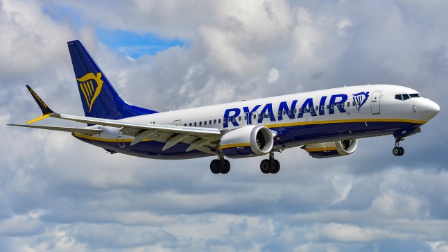A Ryanair plane flying with a cloudy sky in the background.