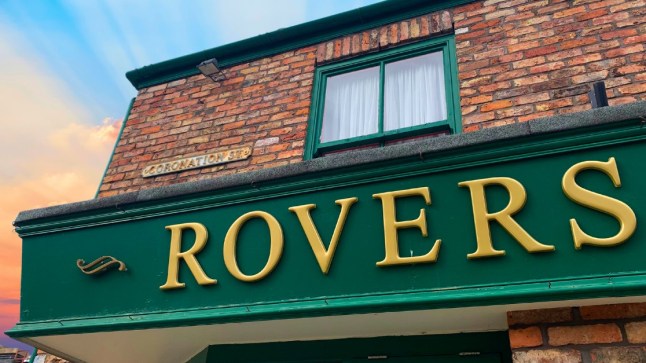 Close-up of the Rovers Return sign in Coronation Street, with a sunset behind.