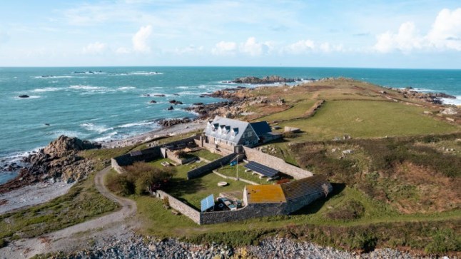 An aerial view of Lihou House in Guernsey, on a rocky island next to the sea.