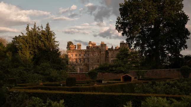 The exterior of Hawarden Castle and its garden on a cloudy day, with a tall tree towering over the castle.