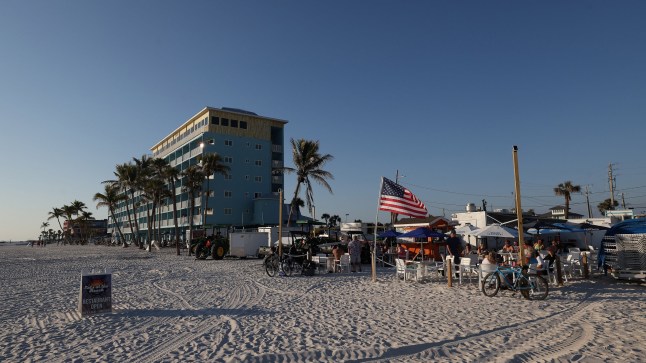 A beachfront in Fort Myers, Florida, with palm trees and an American flag flying in the breeze