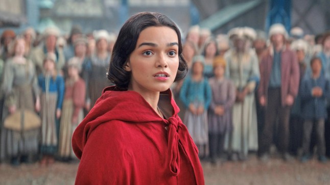 Rachel Zegler as Snow White. She is standing in front of a crowd of people wearing a red cape