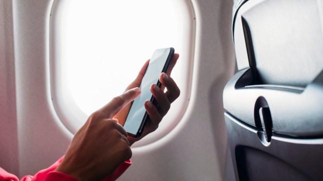 A close up of a woman's hand holding a phone in front of a plane window.