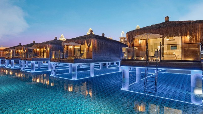 A row of overwater villas as Granada Luxury Belek, Turkey, lit from inside at dusk.