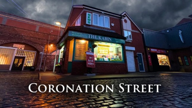 The Kabin on Coronation Street under a gloomy night sky with the Corrie logo in front of it
