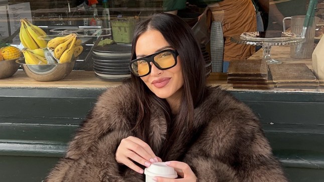 Sarah Ashcroft in a fluffy fur jacket, holding a coffee cup and looking at the camera.