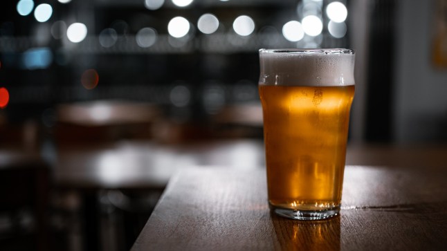 A delicious-looking pint of top-fermented beer sits on a rustic wooden table in a pub. The background features bokeh circles from the lights, creating a warm and inviting atmosphere.