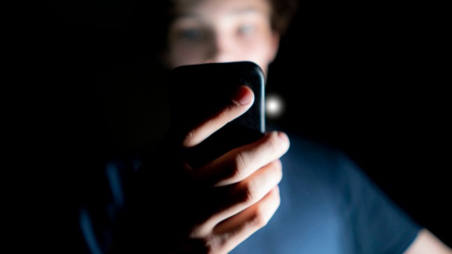 young attractive man use mobile phone late at night in a dark room