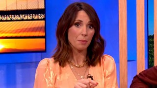 Alex Jones wearing an orange blouse and looking serious on The One Show