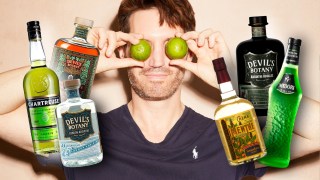 Rob Buckhaven holding limes up to his eyes, surrounded by bottles of absinthe