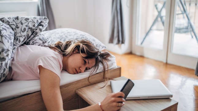 Young woman is waking up and looking at her smart phone.