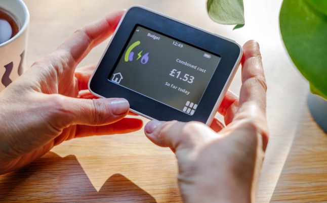 An overhead view of hands holding a home smart meter against a sunlit desk background and checking energy consumption