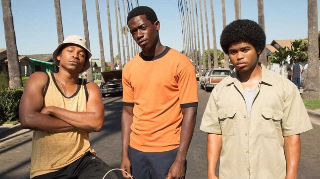 Damson Idris in Snowfall, standing next to two other men on a road flanked by palm trees.