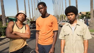 Damson Idris in Snowfall, standing next to two other men on a road flanked by palm trees.
